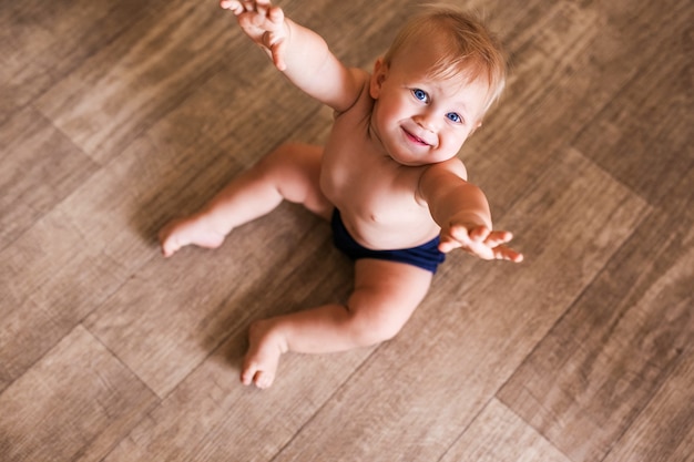 Retrato de un niño de un año sentado en el suelo de madera. Niño bonito en casa