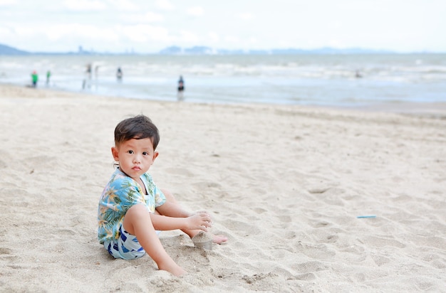 Retrato de niño asiático divirtiéndose con arena en la playa