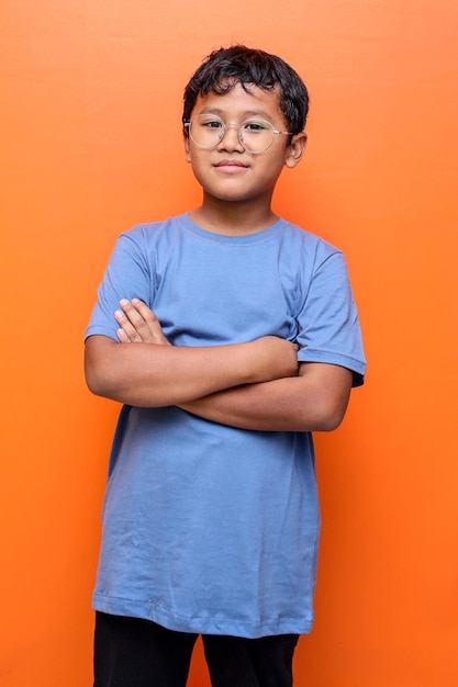 Retrato de un niño asiático sonriente con anteojos de pie con los brazos cruzados