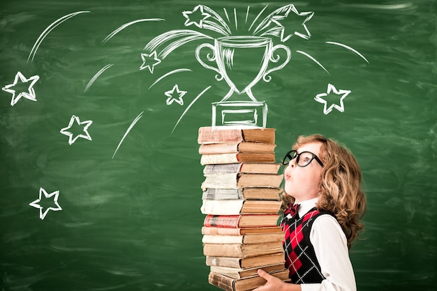 Retrato de niño en el aula contra la pizarra. Niño con libros en clase. Concepto de éxito, idea y victoria. De vuelta a la escuela