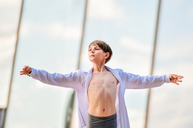 Retrato de un niño de ballet haciendo ejercicio sobre un fondo de cielo reflejo en la pared de vidrio