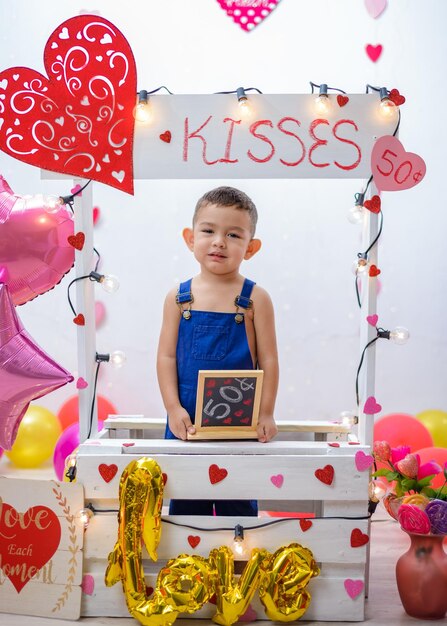 retrato, de, un, niño, en, un, cabina de besos, adornado, con, corazones, y, globos