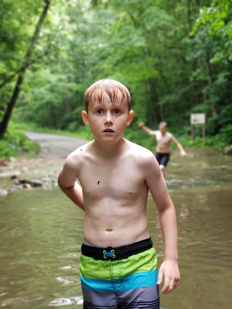 Retrato de un niño sin camisa de pie contra un arroyo en el bosque