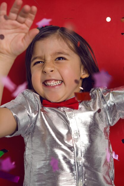 Foto retrato de un niño con una camisa plateada y una corbata roja atrapa confeti brillante en las vacaciones