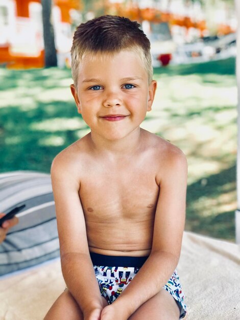 Retrato de un niño sin camisa sentado junto a la piscina