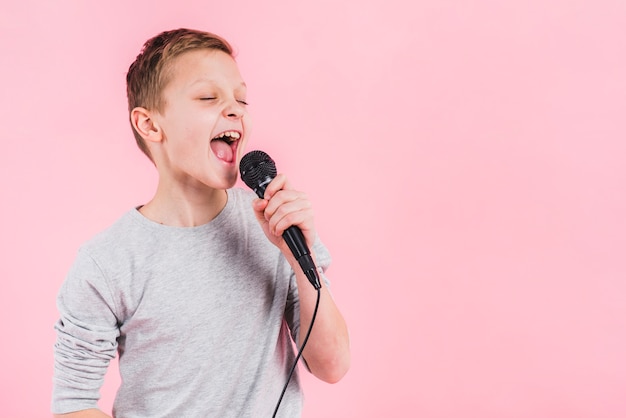 Foto retrato de un niño cantando canción en el micrófono contra el fondo de color rosa