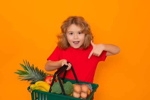 Retrato de niño con carrito de compras lleno de verduras frescas fondo de estudio aislado pequeño chil