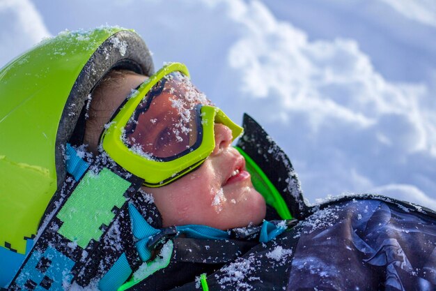Retrato de un niño con casco y gafas de protección tendido en la nieve