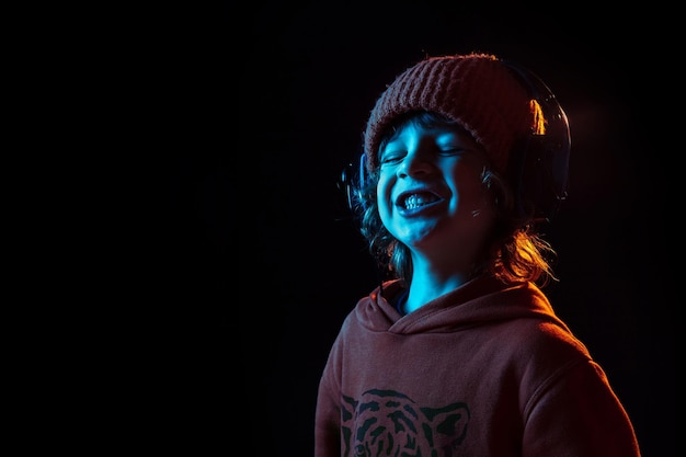 Retrato de niño caucásico aislado sobre fondo oscuro de estudio en luz de neón