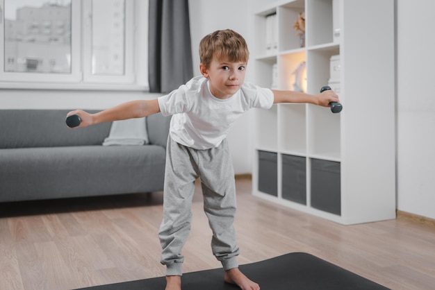 Retrato de niño caucásico haciendo fitness con pesas en casa en la sala de estar.