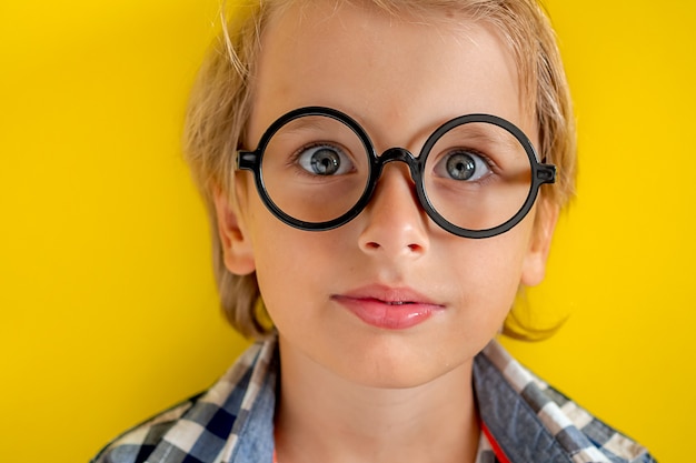 Retrato de niño caucásico rubio lindo e inteligente en una camisa a cuadros sobre fondo amarillo. Día 1 de septiembre. Educación y concepto de regreso a la escuela. Alumno infantil dispuesto a aprender y estudiar.