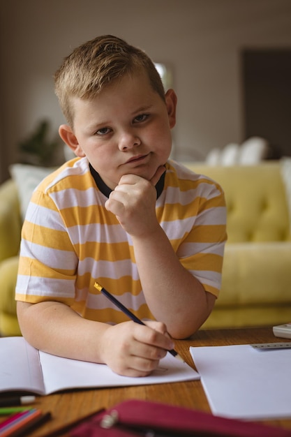 Foto retrato de un niño caucásico sosteniendo un lápiz sentado en la sala de estar de casa