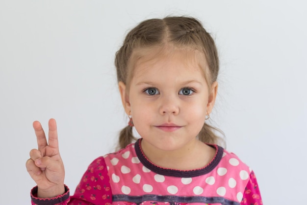 Retrato de un niño caucásico de tres años muestra los dedos para mostrar el número dos o firmar la victoria mirando la cámara en el fondo blanco