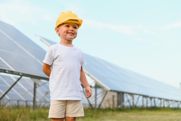 Retrato de un niño cerca de los paneles solares Un niño pequeño con un casco protector cerca de paneles solares con su mano Disparando a una planta de energía solar Granja ecológica Estación de energía solar Gente