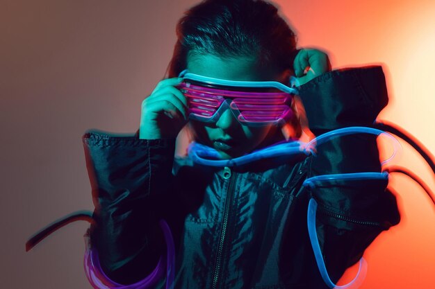 Retrato de niño ciberpunk con gafas de neón en tonos azules y rojos con cables en un fondo rojo