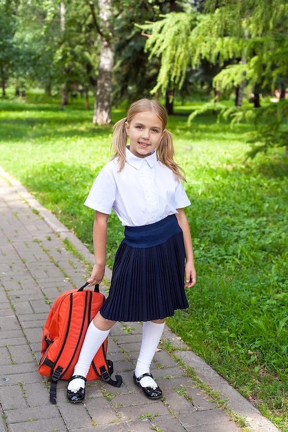 Retrato de un niño-colegiala feliz moderno con una mochila en el parque. La niña sonríe y mira a la cámara.