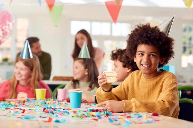 Retrato de niño comiendo pastel de cumpleaños en una fiesta con padres y amigos en casa