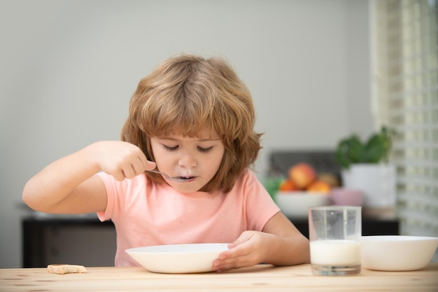 Retrato de un niño comiendo sopa o desayunando almorzando junto a la mesa en casa con una cuchara Comida saludable para niños