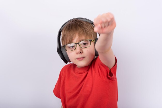 Retrato de niño como superman sosteniendo la mano con el puño hacia arriba. Niño con gafas y auriculares sobre fondo blanco.