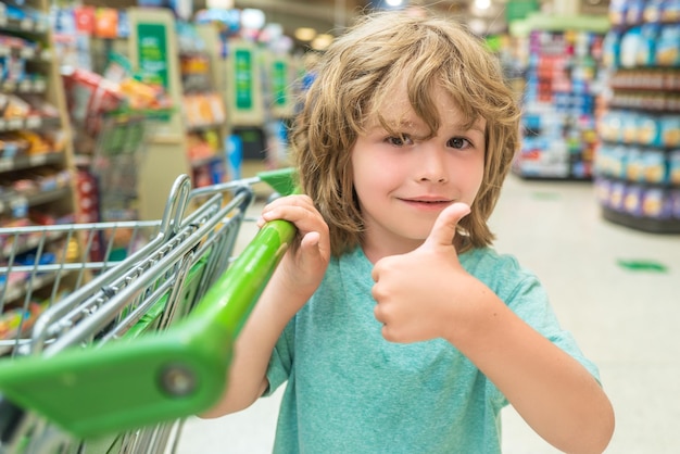 Retrato de niño en compras de comestibles en supermercado Niño con un carrito de supermercado