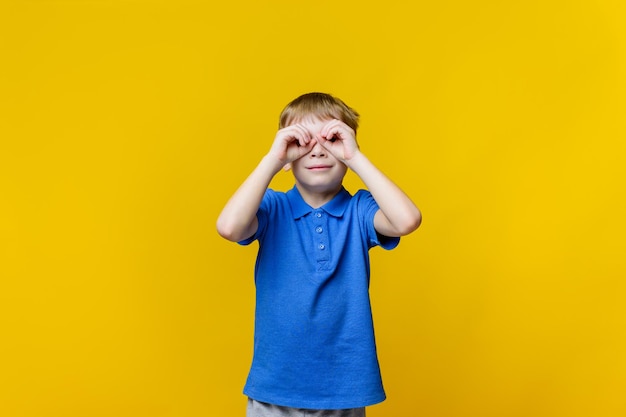 Retrato de un niño curioso mirando a través de los dedos en forma de binoculares fondo amarillo aislado