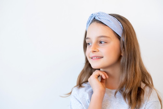 Retrato de niño curioso. Moda infantil. Idea creativa. Una niña sonriente inspirada y pensativa con un accesorio de banda para el cabello de lunares azules mirando el espacio vacío aislado fondo publicitario blanco.