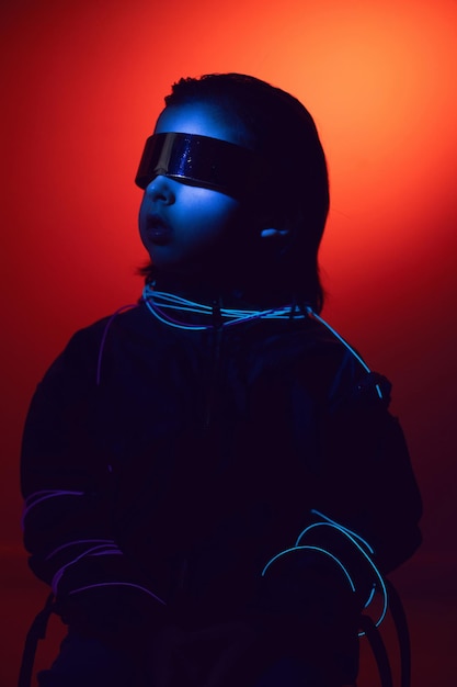 Retrato de niño cyberpunk con gafas vr en tonos azules y rojos con cables en un fondo rojo