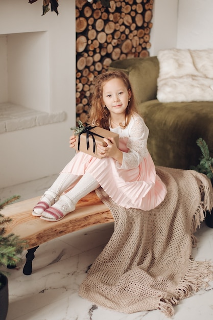 Retrato de un niño dulce en vestido rosa sentado con regalo de Navidad