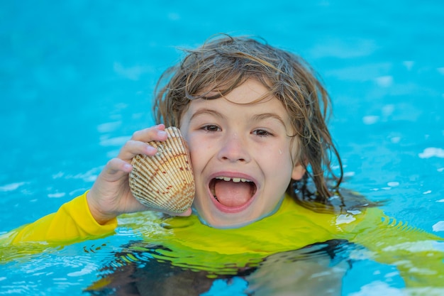 Retrato de niño emocionado sosteniendo conchas marinas nadando en agua de mar Niño lindo jugando con conchas al aire libre en la playa de verano Niño sosteniendo una concha marina Concepto de vacaciones de verano