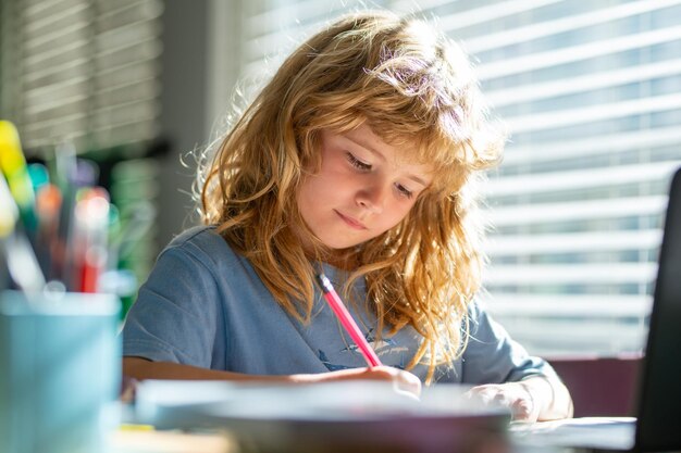 Retrato niño de la escuela sentado en la mesa haciendo los deberes niño serio concentrado escribiendo en el cuaderno fo