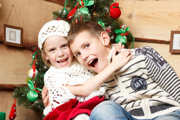 Retrato de niño feliz en el abrazo de su hermana mirando a la cámara en la noche de Navidad