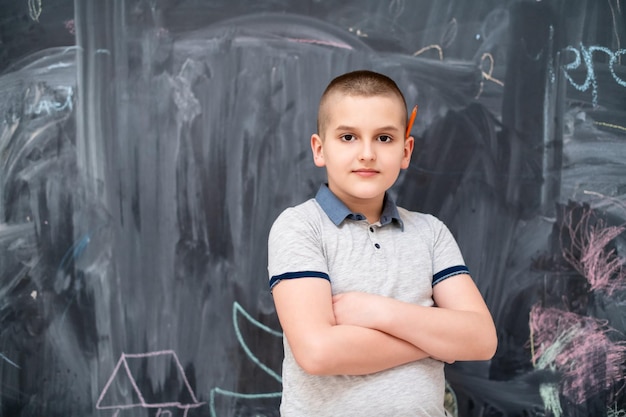 retrato de un niño feliz con un bolígrafo de madera naranja detrás de la oreja parado frente a una pizarra negra