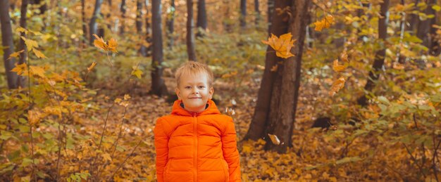 Retrato de niño feliz en chaqueta naranja en el parque de otoño. Temporada de otoño y concepto de niños. Copyspace y espacio vacío para publicidad.