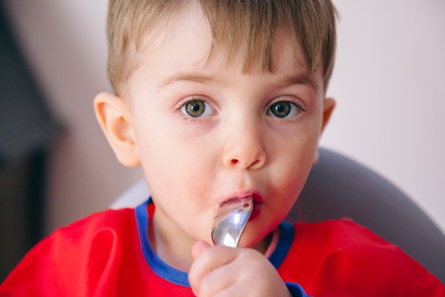 Retrato de un niño feliz chupando una cuchara. Estilo de vida familiar y dieta saludable.