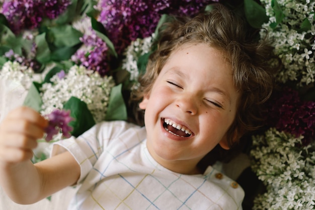 Retrato de un niño feliz en flores lilas. Infancia feliz. Tiempo de primavera