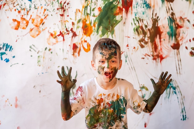 Retrato de niño feliz jugando con acuarela. Rostro y ropa infantil pintados al azar con pinturas. Concepto de diversión infantil, juegos de arte y vandalismo. Imagen en color para el festival holi. Copia espacio