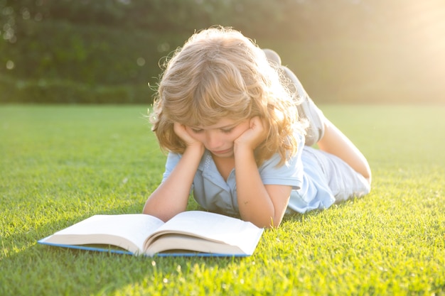 Retrato de niño feliz con libro en el parque. Educación temprana para niños. Niño leyendo un libro en el jardín. Deberes de vacaciones de verano. Estudiante de preescolar al aire libre. Niño lindo de la escuela primaria.