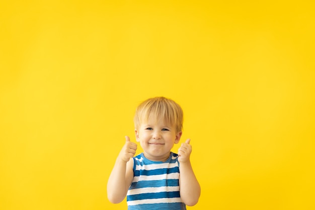 Retrato de niño feliz mostrando los pulgares para arriba contra la pared amarilla en vacaciones de verano.