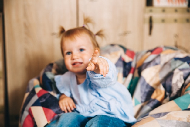 Retrato de un niño feliz, una niña está sentada en una silla suave. Bebé feliz de 1 año.