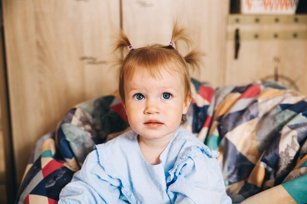 Retrato de un niño feliz, una niña está sentada en una silla suave. Bebé feliz de 1 año.