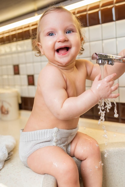 Retrato de un niño feliz que juega y salpica en el fregadero de la cocina