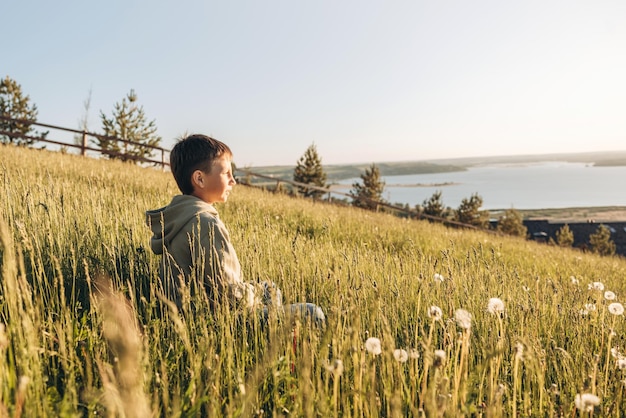 Retrato de niño feliz sentado en la cima de la colina en el campo de hierba y disfrutando del hermoso paisaje al atardecer Adolescente excursionista descansando en la naturaleza Estilo de vida activo Concepto de viaje local