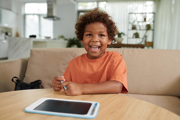 Retrato de un niño feliz sentado en una mesa dibujando en una tableta