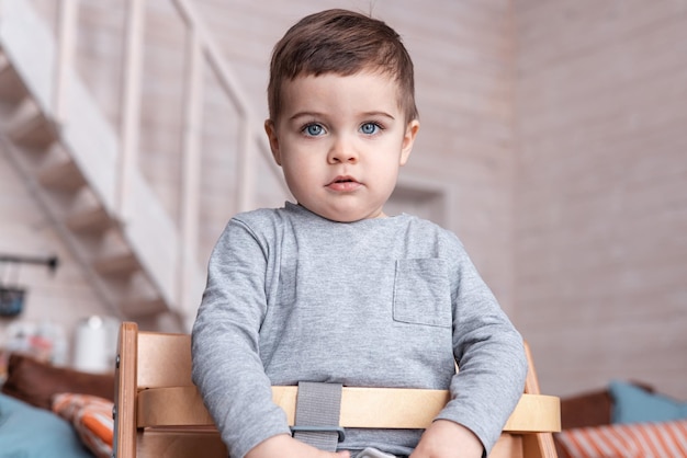 Retrato de un niño feliz en una silla alta Un niño pequeño divertido sentado en una silla alta en casa