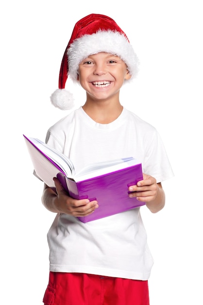 Retrato de un niño feliz con sombrero de Papá Noel con un libro aislado sobre un fondo blanco