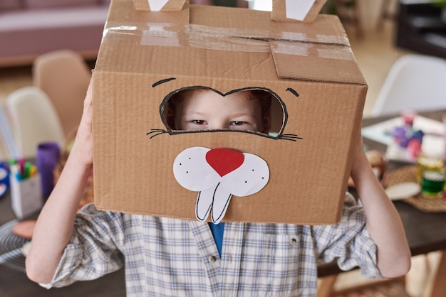 Foto retrato de niño feliz en traje de conejo hecho de caja de cartón sonriendo a la cámara
