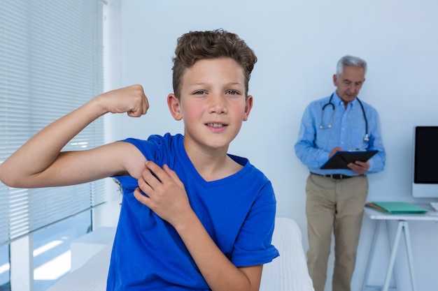 Retrato de niño flexionando sus bíceps en la clínica