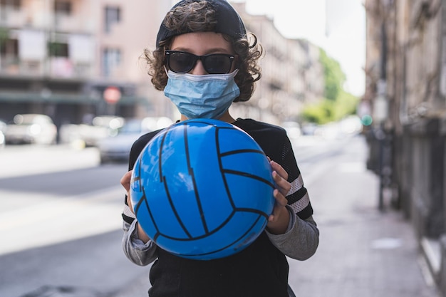 Foto retrato de un niño con gafas de sol sosteniendo una pelota mientras está de pie en la calle