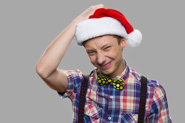 Retrato de niño gracioso feliz con sombrero de Santa. Cierre de chico adolescente con sombrero de Navidad posando sobre fondo gris. Feliz navidad y próspero año nuevo.