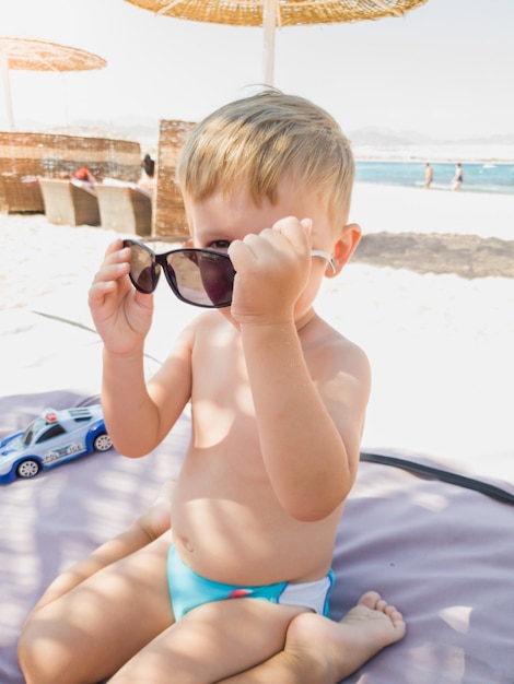 Retrato de niño gracioso jugando y probándose gafas de sol en la playa del mar